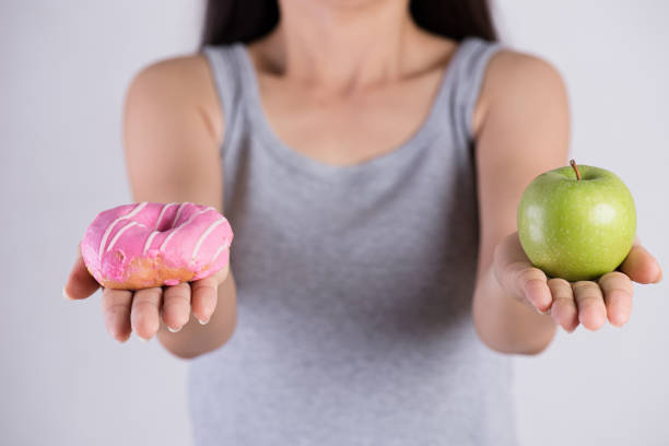 gesundes lifestyle-, ernährungs- und sportkonzept. gesund versus ungesund. frau hand hält donut und grünen apfel. - ungesund leben stock-fotos und bilder