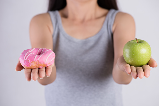 Healthy lifestyle, food and sport concept. Healthy versus unhealthy. Woman hand holding donut and green apple.
