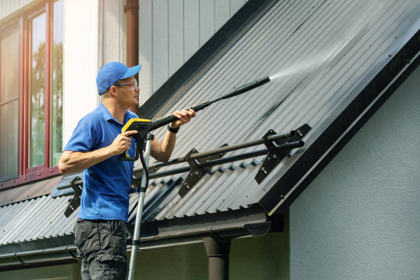 man standing on ladder and cleaning house metal roof with high pressure washer stock photo