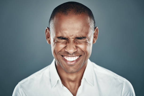 istock So happy! Charming young African man in shirt squinting and smiling while standing against grey background 1160970546