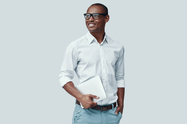 istock Smart and young. Handsome young African man using digital tablet and smiling while standing against grey background 1160973728