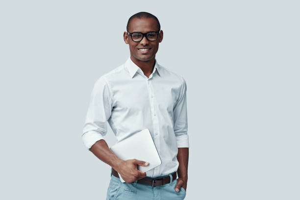 istock Smart and charming. Handsome young African man using digital tablet and looking at camera while standing against grey background 1160973756