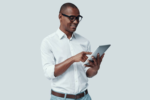istock Examining new tablet. Handsome young African man using digital tablet and smiling while standing against grey background 1160974016