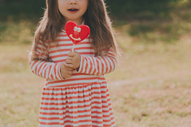 赤いハート型のキャンディを持つかわいい女の赤ちゃん。 - child valentines day candy eating ストックフォトと画像