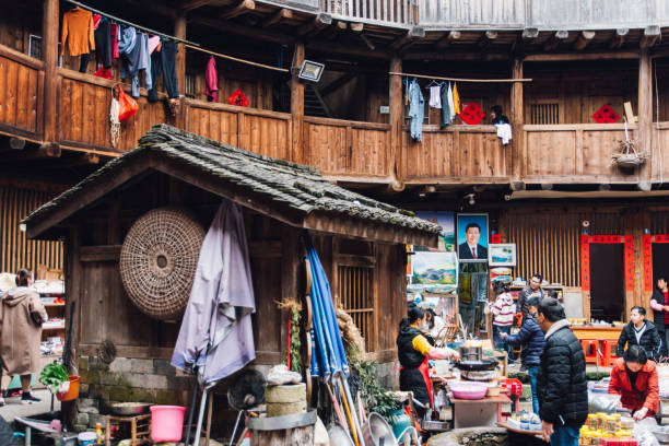 The picture of Xi Jinping is hidden in Fujian tulou. The picture of Xi Jinping is hidden in Fujian tulou.

The Fujian tulou are Chinese rural dwellings unique to the Hakka in the mountainous areas in southeastern Fujian, China. They were mostly built between the 12th and the 20th centuries.

A tulou is usually a large, enclosed and fortified earth building, most commonly rectangular or circular in configuration, with very thick load-bearing rammed earth walls between three and five stories high and housing up to 800 people. Smaller interior buildings are often enclosed by these huge peripheral walls which can contain halls, storehouses, wells and living areas, the whole structure resembling a small fortified city.

The fortified outer structures are formed by compacting earth, mixed with stone, bamboo, wood and other readily available materials, to form walls up to 6 feet (1.8 m) thick. Branches, strips of wood and bamboo chips are often laid in the wall as additional reinforcement. The result is a well-lit, well-ventilated, windproof and earthquake-proof building that is warm in winter and cool in summer. Tulous usually have only one main gate, guarded by 4–5-inch-thick (100–130 mm) wooden doors reinforced with an outer shell of iron plate. The top level of these earth buildings has gun holes for defensive purposes. xi jinping stock pictures, royalty-free photos & images