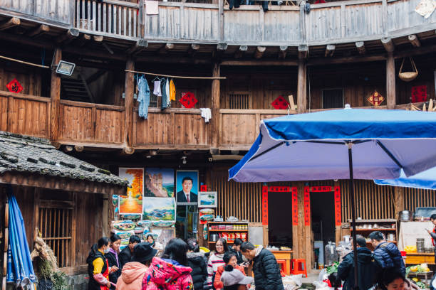 The picture of Xi Jinping is hidden in Fujian tulou. The picture of Xi Jinping is hidden in Fujian tulou.

The Fujian tulou are Chinese rural dwellings unique to the Hakka in the mountainous areas in southeastern Fujian, China. They were mostly built between the 12th and the 20th centuries.

A tulou is usually a large, enclosed and fortified earth building, most commonly rectangular or circular in configuration, with very thick load-bearing rammed earth walls between three and five stories high and housing up to 800 people. Smaller interior buildings are often enclosed by these huge peripheral walls which can contain halls, storehouses, wells and living areas, the whole structure resembling a small fortified city.

The fortified outer structures are formed by compacting earth, mixed with stone, bamboo, wood and other readily available materials, to form walls up to 6 feet (1.8 m) thick. Branches, strips of wood and bamboo chips are often laid in the wall as additional reinforcement. The result is a well-lit, well-ventilated, windproof and earthquake-proof building that is warm in winter and cool in summer. Tulous usually have only one main gate, guarded by 4–5-inch-thick (100–130 mm) wooden doors reinforced with an outer shell of iron plate. The top level of these earth buildings has gun holes for defensive purposes. xi jinping stock pictures, royalty-free photos & images