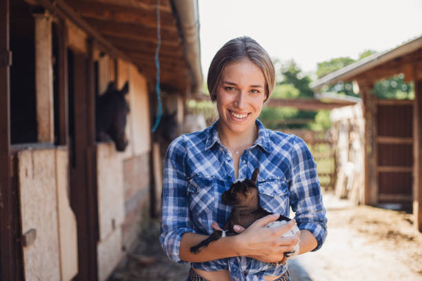 Toothy smiling cowgirl and her newborn little goat Cowgirl and her farm newborn animal newborn horse stock pictures, royalty-free photos & images