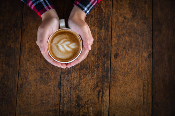 Woman hand holding a cup of coffee on an old wooden table, top view