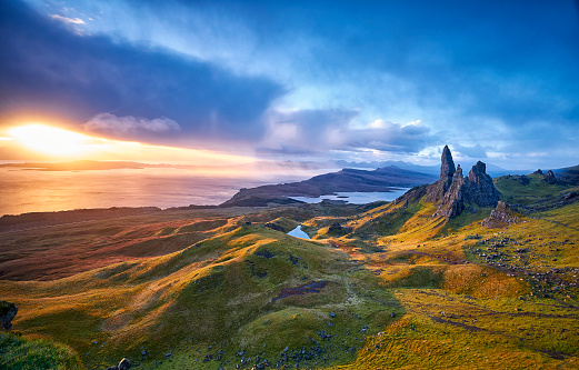 View Over Old Man Of Storr, Isle Of Skye, Scotland. During a beautiful sunrise and dramatic sky with a local shower here and there. The Old Man of Storr looms over Portree, Isle of Skye and is situated 7 miles north of the town. It is dominated by the 50 metre high petrified lava pinnacle of the Old Man of Storr, with a brutal tumble of cliff behind, and the panorama spreads across loch, sea and islands to the high mountains of the mainland beyond.