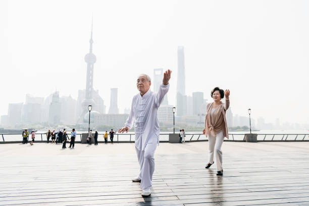 Poised senior Chinese couple doing Tai Chi on The Bund with Pudong cityscape landmarks in the background.
