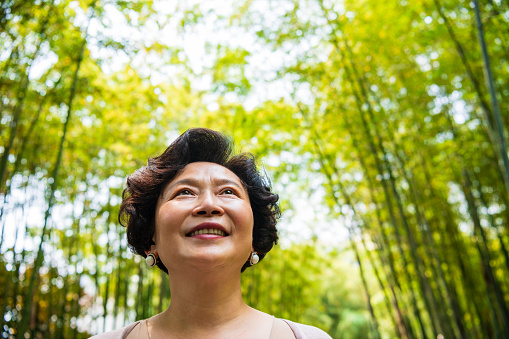 Portrait of a smiling senior Chinese woman pausing to enjoy the natural beauty of a Shanghai bamboo grove.