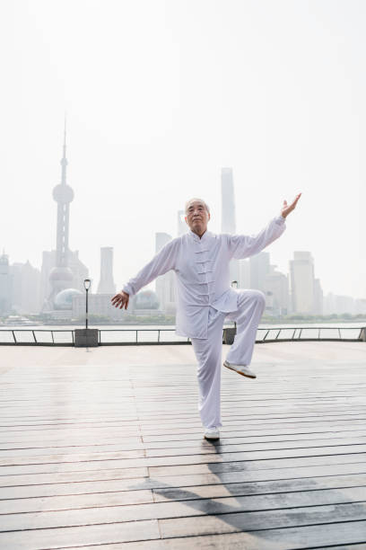 Graceful Senior Chinese Man Doing Tai Chi on the Bund Perfectly balanced senior Chinese man in traditional white uniform holding a Tai Chi pose on The Bund with Pudong in the background. view into land stock pictures, royalty-free photos & images