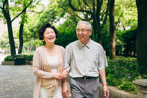 Cheerful senior Chinese couple spending a sunny spring day talking and walking through a Shanghai park.