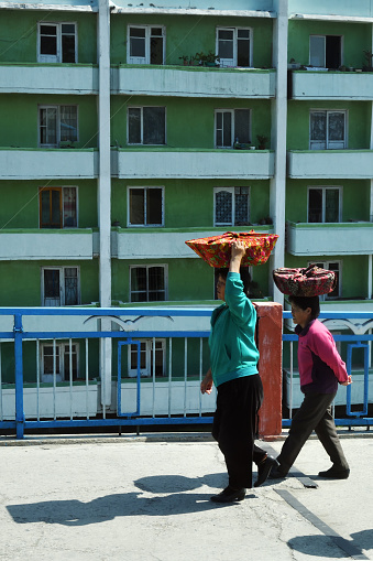 Wonsan, North Korea - May 3, 2019:  Street scene   in Wonsan, North Korean port on Eastern seashore. Two women carry baskets on their heads
