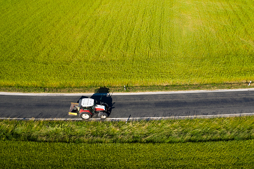 Tractor on country road between fields in summer, viewed from above.