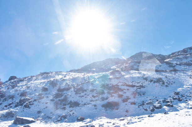 sole in cima alla copertura di neve della catena himalayana. il picco roccioso ghiacciato pieno di neve profonda illumina la luce del sole nascente nel gelido giorno invernale. cielo blu chiaro. niente cloud. percorso verso il sole. pittoresca bellezza del - european alps cold mountain range clear sky foto e immagini stock