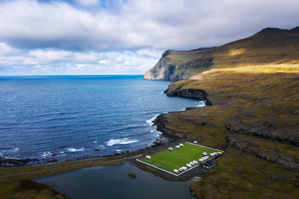 Aerial view of an old football field on the coast near Eidi in Faroe Islands Aerial view of an old football field with scenic cliffs in the background located on the coast near the village of Eidi in Faroe Islands, Denmark. This football stadium is now used as a campsite. faroe islands photos stock pictures, royalty-free photos & images