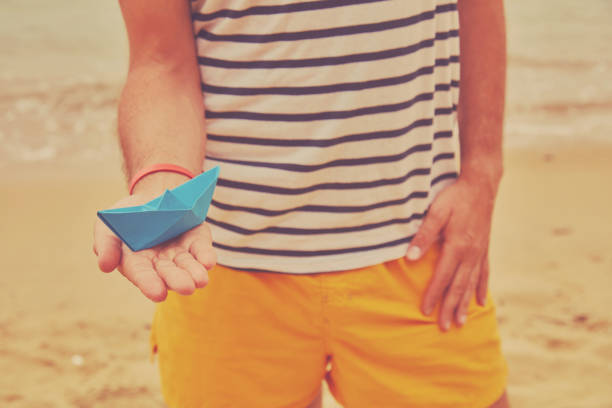 istock Man holding paper boat on tropical beach. 1160985666