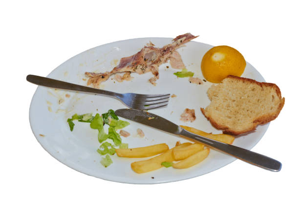 Empty plate with fork and knife and leftover food, isolation on white