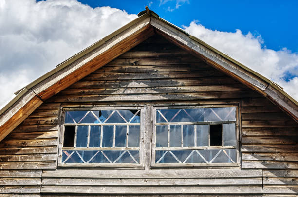 gable end di un cottage invecchiato con rivestimenti orizzontali in legno e finestre in una giornata di sole. nuvole bianche e sfondo cielo blu. - gable end foto e immagini stock