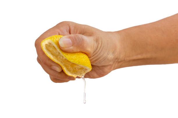 istock Women's hand squeezing a half of fresh lemon yellow on a white background. 1160996697