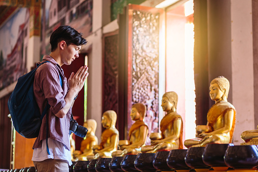 Young Asian traveller man travel with backpack respecting or pray at Wat Nong Waeng temple, Khonkaen, Thailand