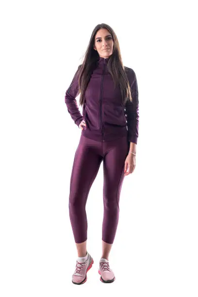 Relaxed smiling long hair brunette fit woman in tracksuit posing and looking at camera. Full body isolated on white background.
