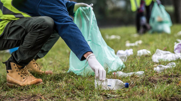 Picking up a plastic bottle during park clean-up Unrecognizable volunteer picking up a plastic bottle during a park clean-up action. reflective clothing photos stock pictures, royalty-free photos & images