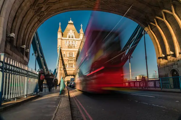 Beautiful long exposure with blurred motion at Tower Bridge in City of London, UK. Dragged exposure technique to capture the busy road traffic (red double decker bus)and constant commuters and tourist (unrecognisable people) visiting this famous international landmark, connecting City of London directly to the Southwark bank (Unesco heritage site nowadays and build in 1894) . Shot on Canon EOS R full frame system with premium RF lens for highest quality results from a tripod on a sunny day with clear blue sky.