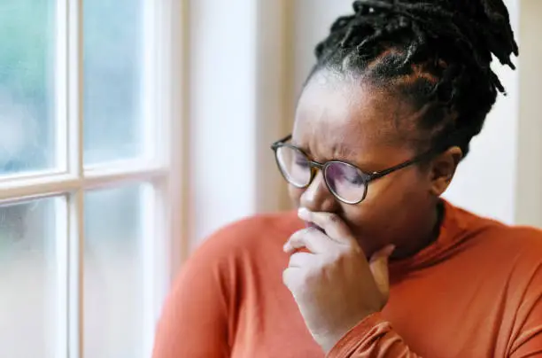 Close-up of a sad afro american woman crying while sitting by a window at home