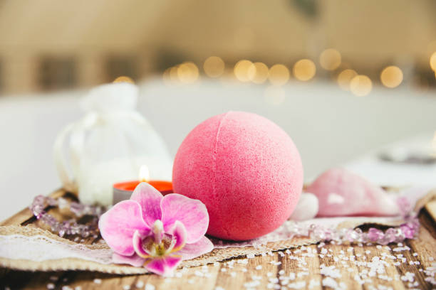 Pink bath ball with orchid flower, scented candle and bath salt on wooden tray in bath room. Therapy concept. Taking a relaxing bath. Pink bath ball with orchid flower, scented candle and bath salt on wooden tray in bath room. Therapy concept. Taking a relaxing bath. bath salt photos stock pictures, royalty-free photos & images