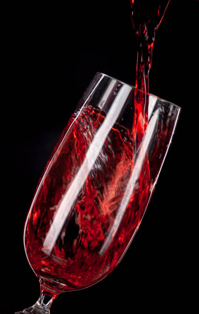 istock Red wine pouring into a wine glass. Isolated on black background. 1161018268