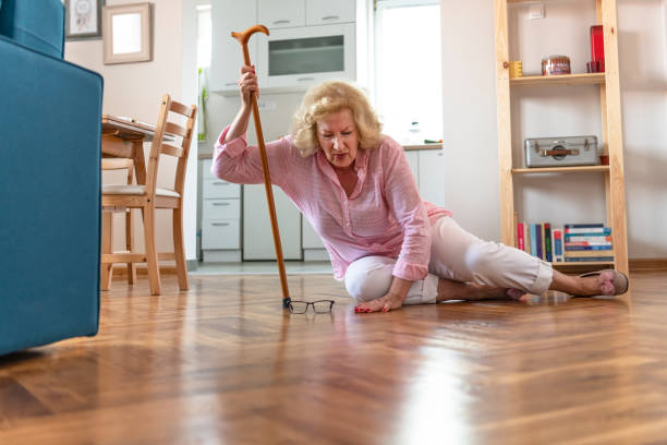 mujer jubilada despiacada con el pelo rubio sentada en el suelo en casa. los riesgos que conllevan envejecer. - fell down fotografías e imágenes de stock