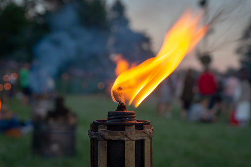Burning flame of an outdoor torch at a party at dusk with a group of blurred people in the background celebrating at sunset