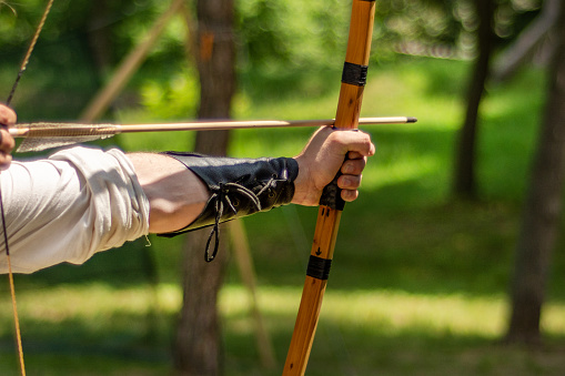 Strong man archer hand holds his bow with an arrow and aiming at the target outdoor activity in forest. Medieval sport concept. Close up, selective focus