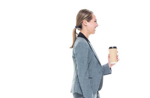 Attractive businesswoman wearing a grey suit - walking and holding a briefcase and coffee cup
