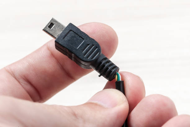 Broken black usb cable at hand on a wooden background. old wire with dust. holding broken usb transfer or charging wire. how to repair broken wires.