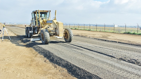 Construction Blade Grading Rock for a New Roadway in Perris California. March Air force Base is in the Back Ground. There is a Survey Level on the left side