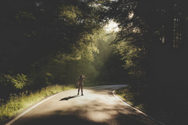 istock Dark forest road. Man on the road in sunlight 1161042894