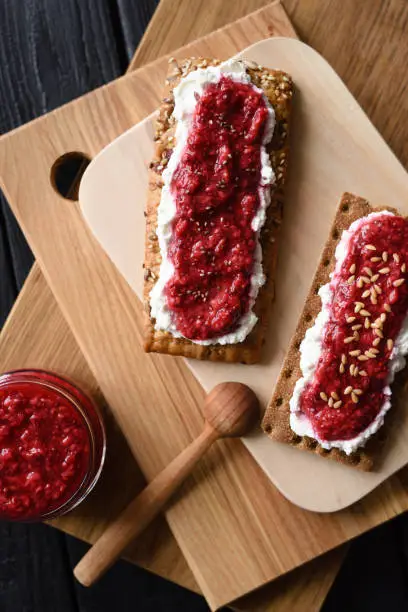 Superfood dessert flat lay. Chia seed raspberry jam with flax seeds and ricotta on wholegrain crispbread on wooden boards copy space