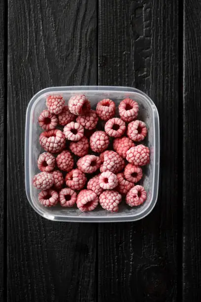 Freezing berries. Frozen raspberries in container on black background copy space