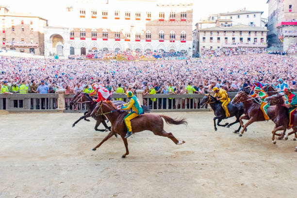 Horses competing during the first lap of the 2019 Palio di Siena in the "Piazza di Campo" at the city of Siena in Tuscany, Italy. Horses competing during the first lap at the "Piazza di Campo" at the city of Siena in Tuscany, Italy, during the July 2nd, 2019 "Palio di Siena" known locally as "Il Palio", a traditional horse race held twice a year in July and August since 1656. Ten horses representing ten of the seventeen districts ("Contradas") with jockeys riding bareback compete during a three-lap race around a makeshift course built in the the city's central square. torre del mangia stock pictures, royalty-free photos & images