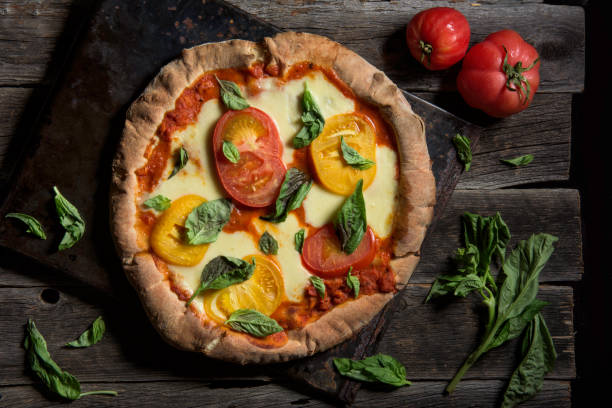 Artisan Basil and Tomato Pizza A gourmet pizza with basil and heirloom tomatoes surrounded by ingredients artisanal food and drink stock pictures, royalty-free photos & images