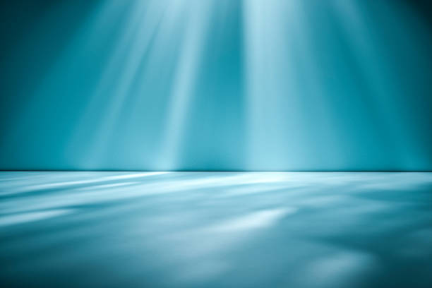 Beams of sunlight on a blue green studio background wall casting dappled light on the floor in an empty room for product placement or interior design themes