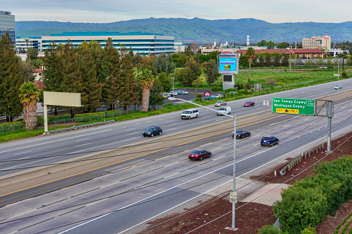 Santa Clara, California, USA - March 31, 2019: Aerial bird's eye view of light weekend car traffic on eight-lane highway 101 in urban heart of Silicon Valley with green mountain range in background