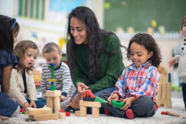 Teacher playing with students A young beautiful teacher is playing with her students. She has a giant smile on her face while she holds a block in her hand. montessori education stock pictures, royalty-free photos & images