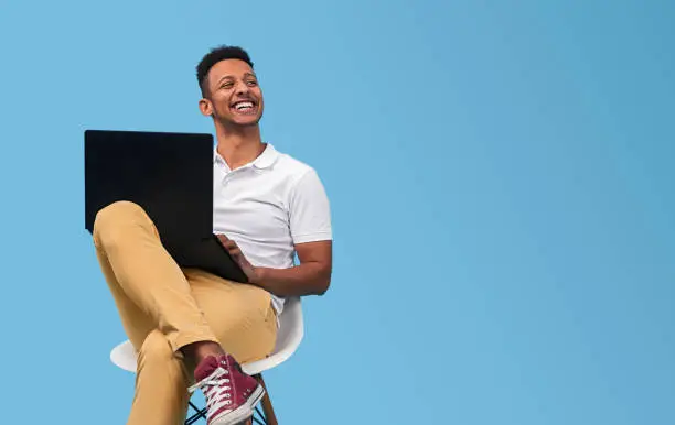 Photo of Cheerful black student with laptop looking away