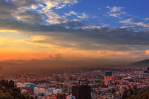 Looking towards the sunset over the capital city of Bogota, Colombia in South America, from the heights of La Calera. The setting sun hits the buildings both tall and small at an oblique angle.  In the distance is some smog near the Andes Mountains.  Horizontal format; copy space.