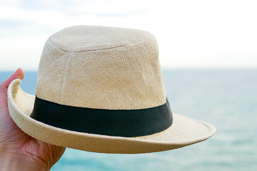 hand is holding panama hat in the blue sea and white sky background that represent relaxing and travel lifestyle
