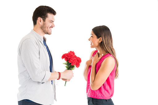 Cheerful young woman receiving flower bouquet from smiling boyfriend against plain background